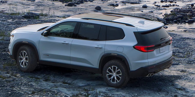 A white Acadia driving a girl on rocky riverbed road